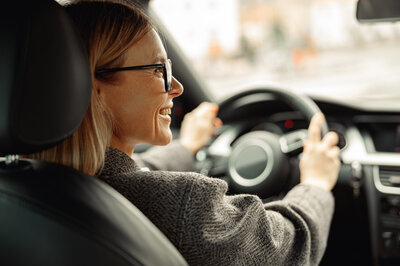 So vergleichst und sicherst Du Dir Dein Auto Abo Eine Frau sitzt freudig am Steuer ihres Fahrzeugs, dass sie mit einem Auto Abo Vergleich gefunden hat.